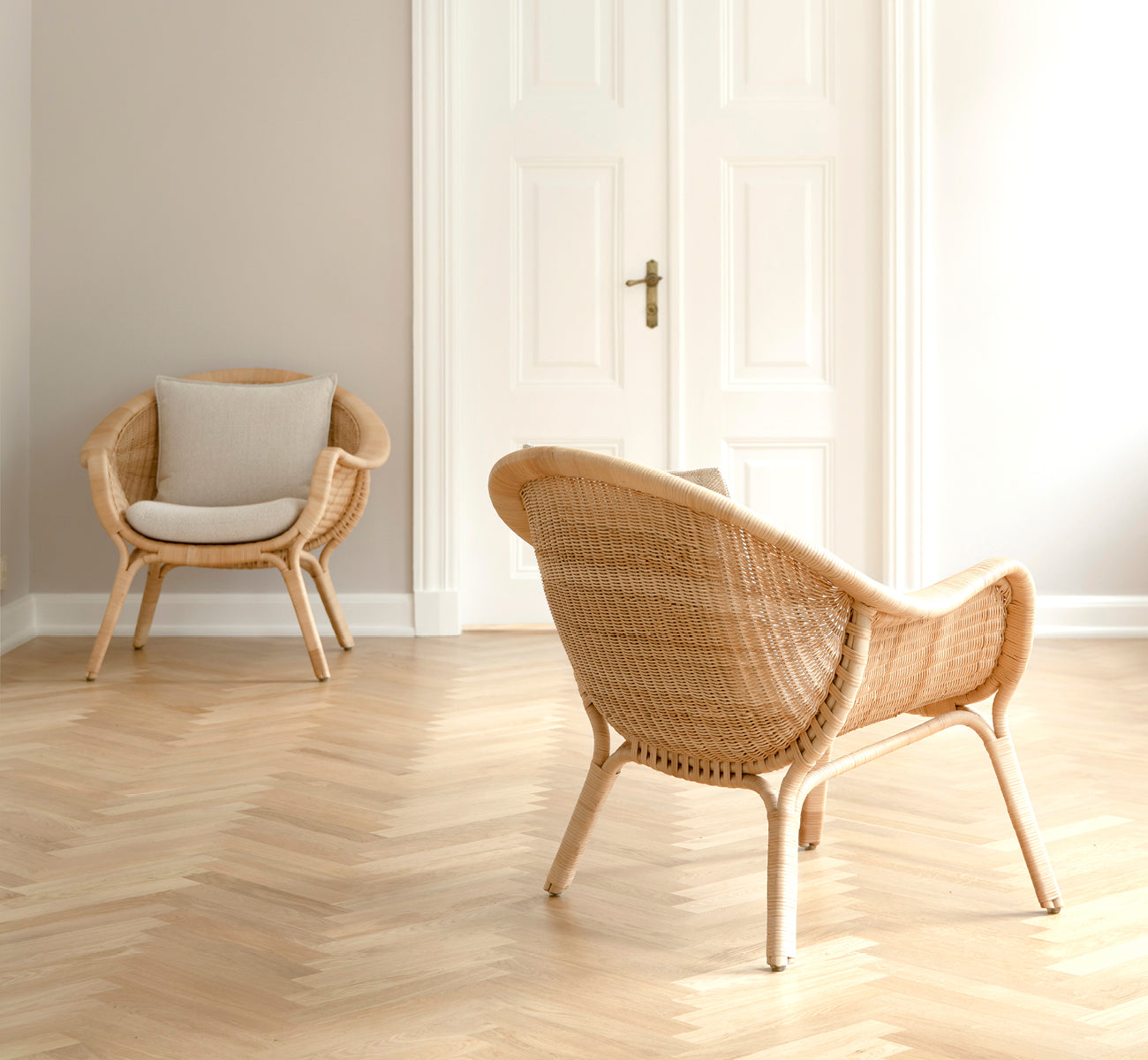 Dette er et livsstilsbillede af Madame Lænestol i natural core weave rattan frame. Lyst rum med sildebensgulv og hvide dobbeltdøre.
