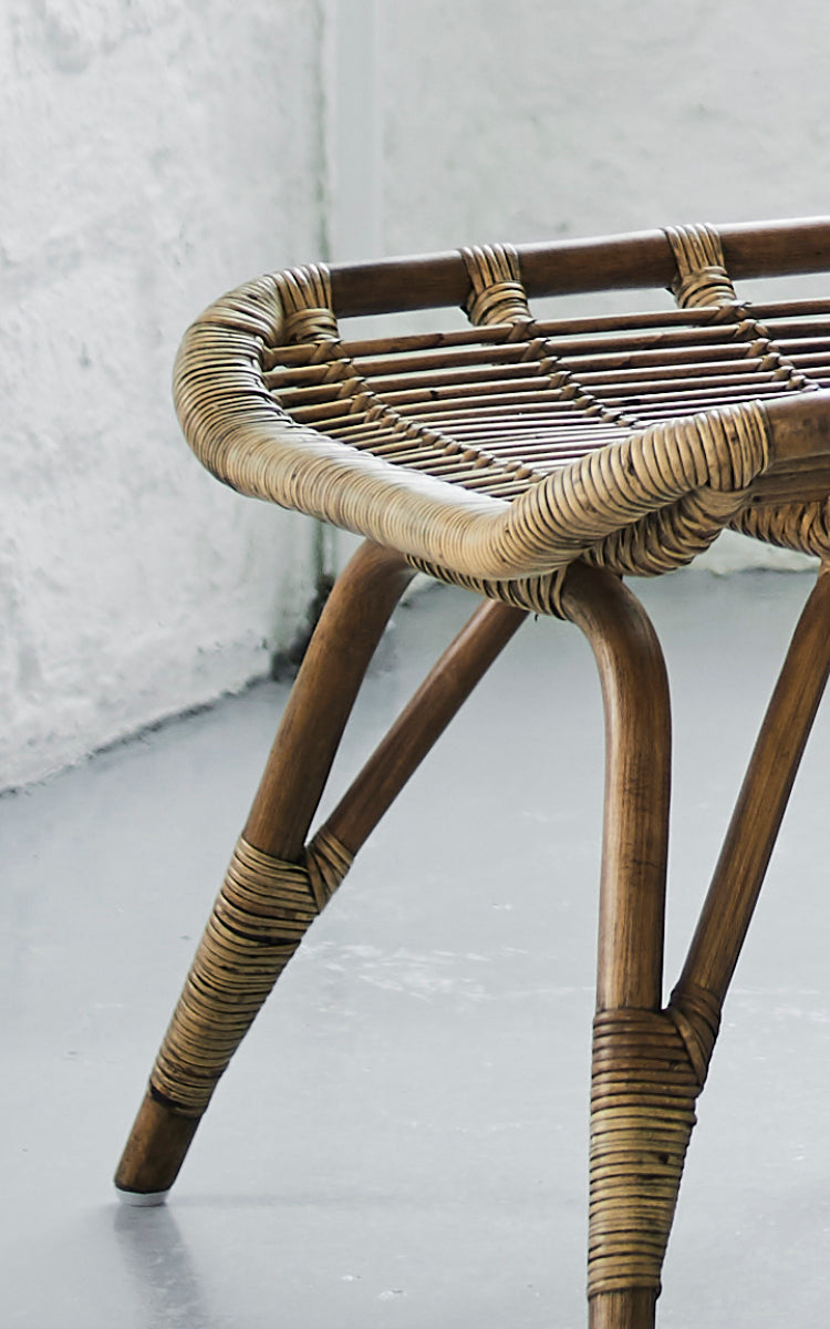 Dette er et nærbillede af Monet Footstool i antique rattan. Detalje af den flade flettede sædeflade og de spredte rattanben.