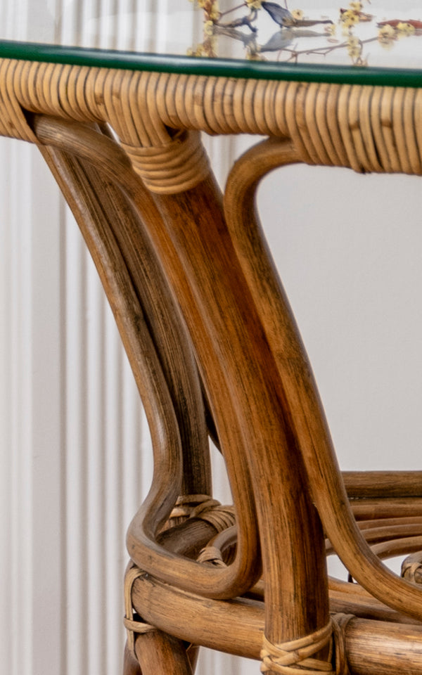 Dette er et nærbillede af Tony Café Table i antique rattan. Detalje af glaspladens kant, buet rattanstel og omviklede samlinger.