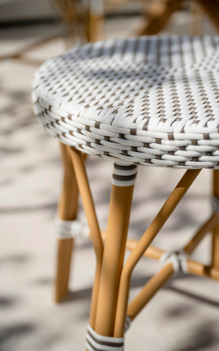 Dette er et nærbillede af Simone Udendørs skammel i almond aluminium frame white w cappuccino dot artfibre. Flettet sæde og omviklede ben i sollys.