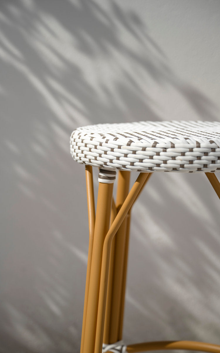Dette er et nærbillede af Simone Udendørs barstol i almond aluminium frame white w cappuccino dot artfibre. Flettet sæde ved en hvid væg.