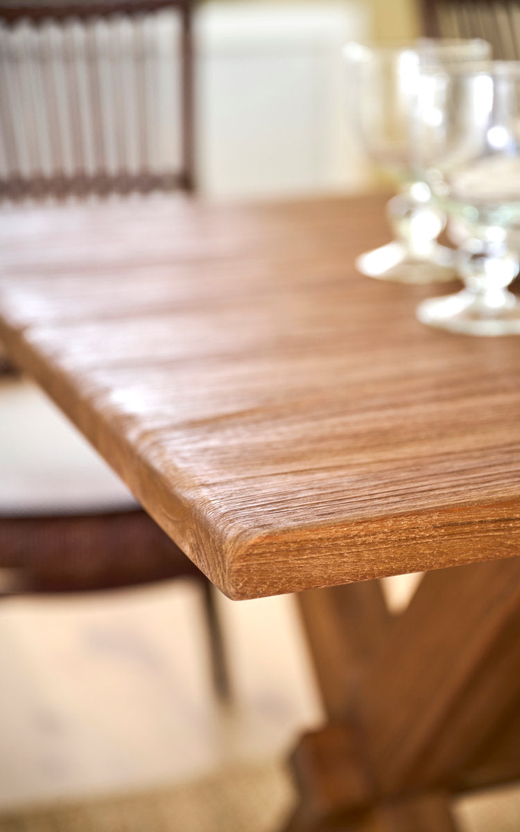 Dette er et nærbillede af Hugo Teak spisebord 180x90 cm i teak indoor. Kant af teakbordplade med glas og rattanstole.