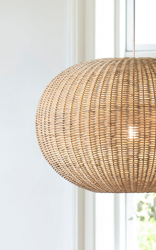 Dette er et nærbillede af Tangelo Lampshade Ø62 cm | Large i natural rattan. Detalje af den store rattanflet på den afrundede pendel ved et vindue.