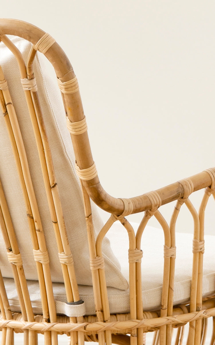 Dette er et nærbillede af Tulip Lænestol i polished natural rattan. Detalje af rattanstellet, buede stivere og linnedpude.