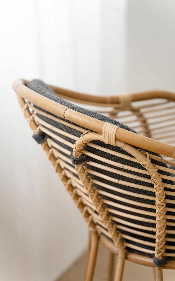 Dette er et nærbillede af Swing Lænestol i polished natural rattan. Detalje af den buede rattan-topskinne og flettede ryglænsbinding.