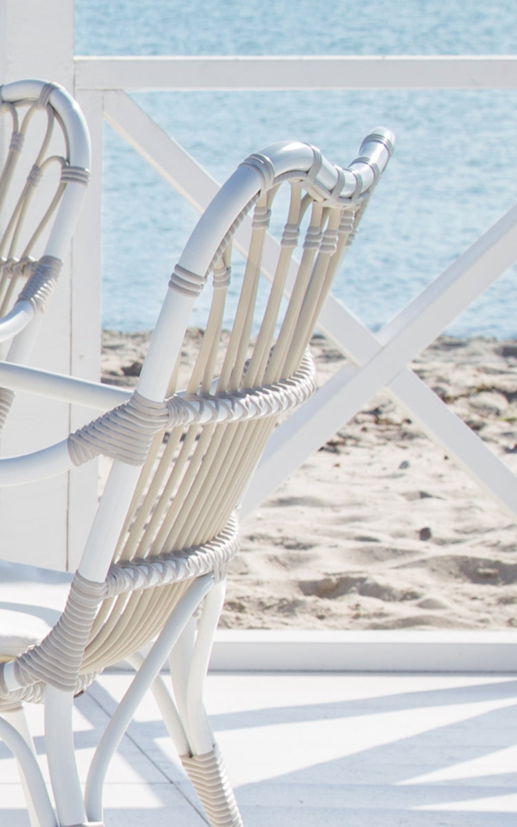 Dette er et nærbillede af Margret Udendørs spisestuelænestol i dove white aluminium artfibre. Hvide buede sprosser med omviklede samlinger ved havet.