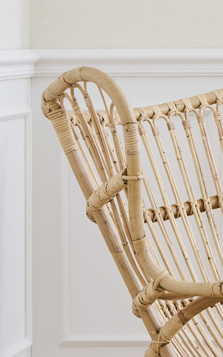 Dette er et nærbillede af Teddy Lænestol i polished natural rattan. Detalje af den buede rattan-topskinne og spindelryg.