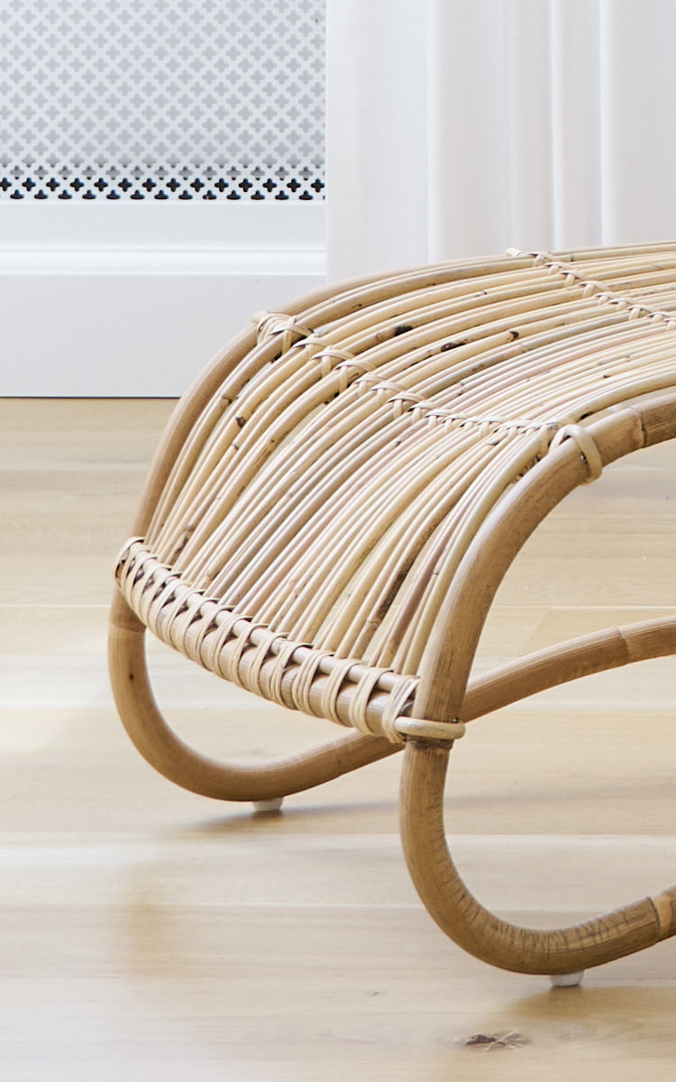 Dette er et nærbillede af Teddy Fodskammel i polished natural rattan. Detalje af de buede rattanskinner og flettede omvikling på fodskammel.