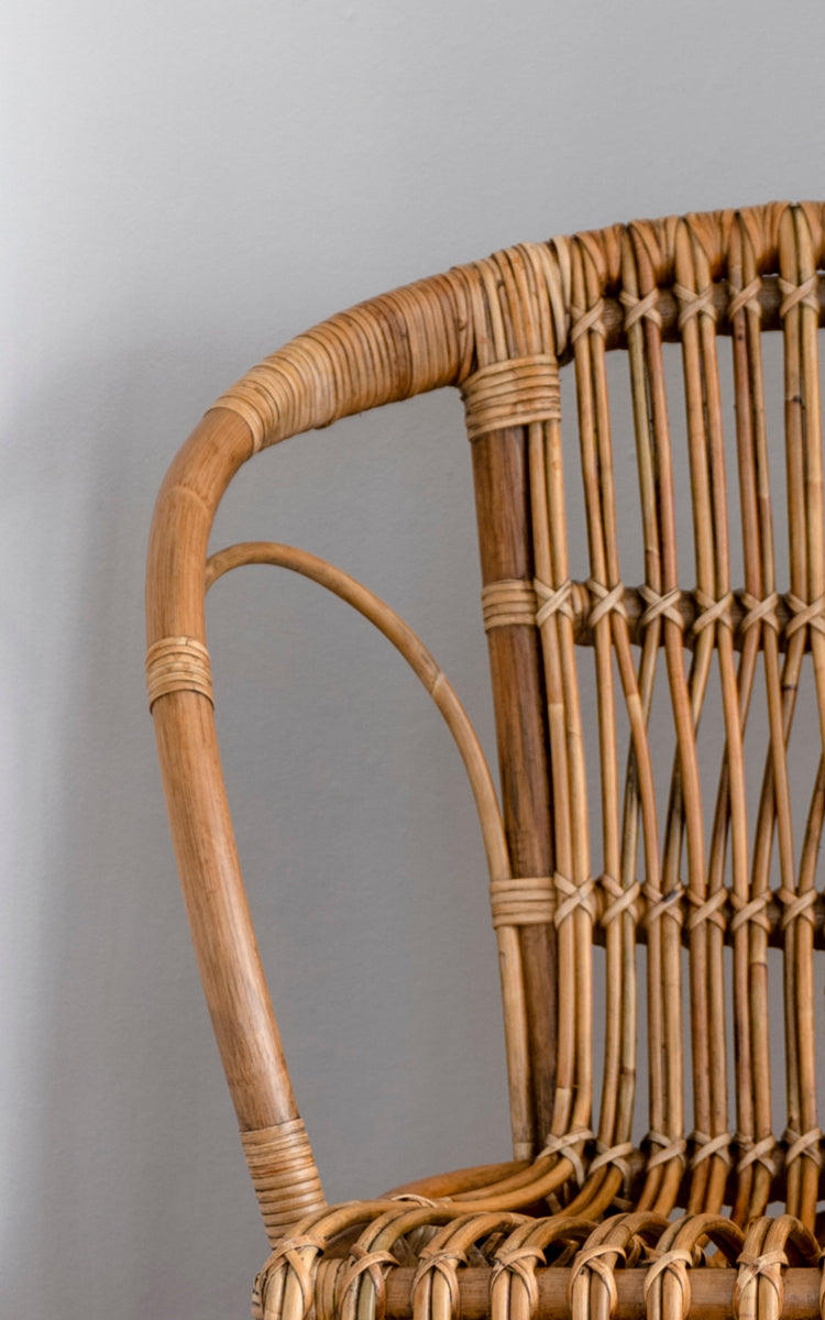 Dette er et nærbillede af Robert Spisebordsstol i polished antique rattan. Detalje af den buede rattan-arm og spindelryg med omviklede samlinger.