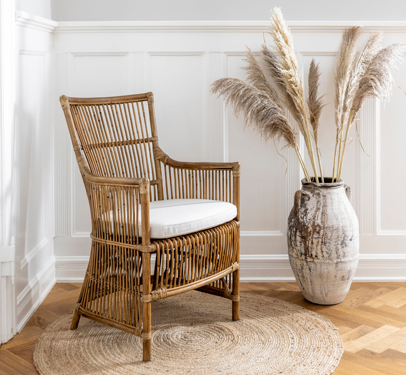 Dette er et livsstilsbillede af Davinci Spisebordsstol i antique rattan, i et lyst interiør med hvide panelvægge og sildebensgulv.