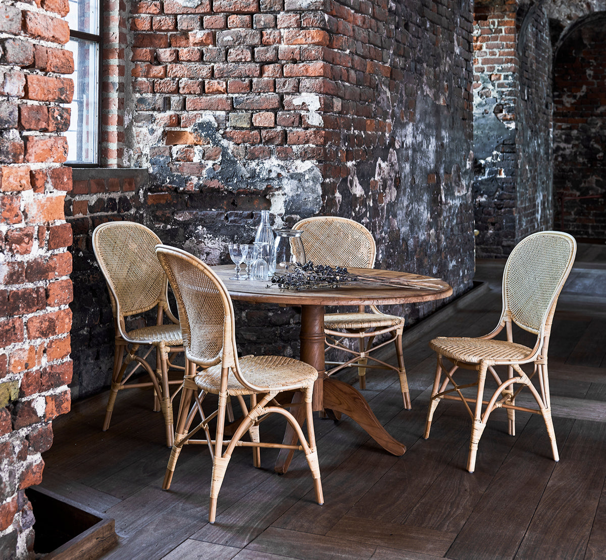 Dette er et livsstilsbillede af Rossini Spisebordsstol i natural rattan. Placeret ved siden af et bistrobord med glasplade på et jutetæppe i et lyst hallway.