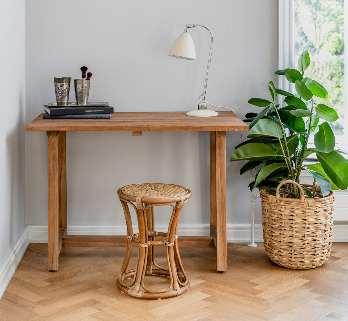 Dette er et livsstilsbillede af Bella Skammel i antique rattan, i et lyst interiør med hvide panelvægge og sildebensgulv.