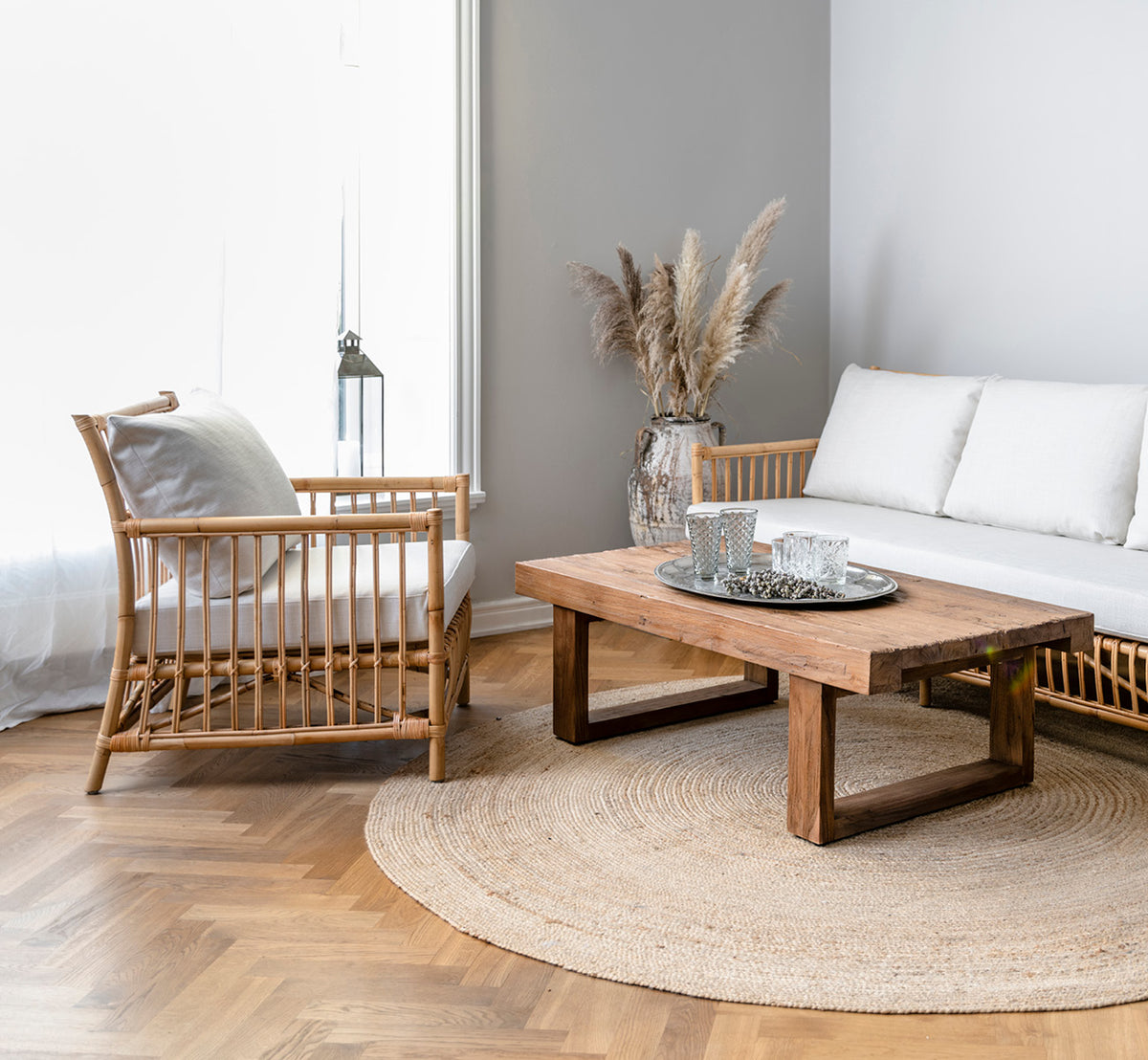 Dette er et livsstilsbillede af Caroline Lænestol i natural rattan, i en lys skandinavisk stue med sildebensgulv.