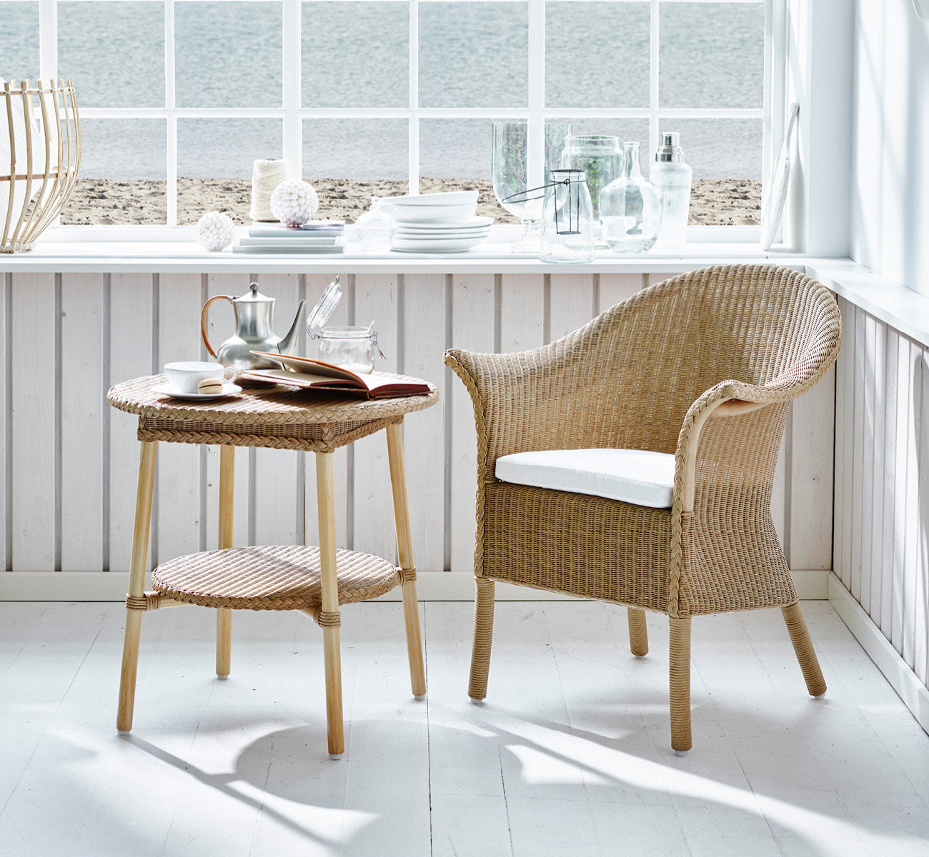 Dette er et livsstilsbillede af Classic Spisebordsstol i natural Loom Rattan Frame, i et lyst interiør med hvide panelvægge og sildebensgulv.