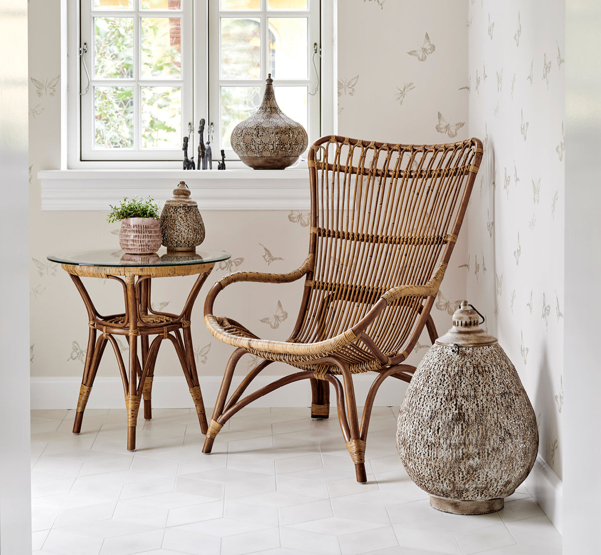 Dette er et livsstilsbillede af Monet Lounge Chair i antique rattan. Med fodskammel i et rustikt hvidt rum med mørkeblåt tekstil.