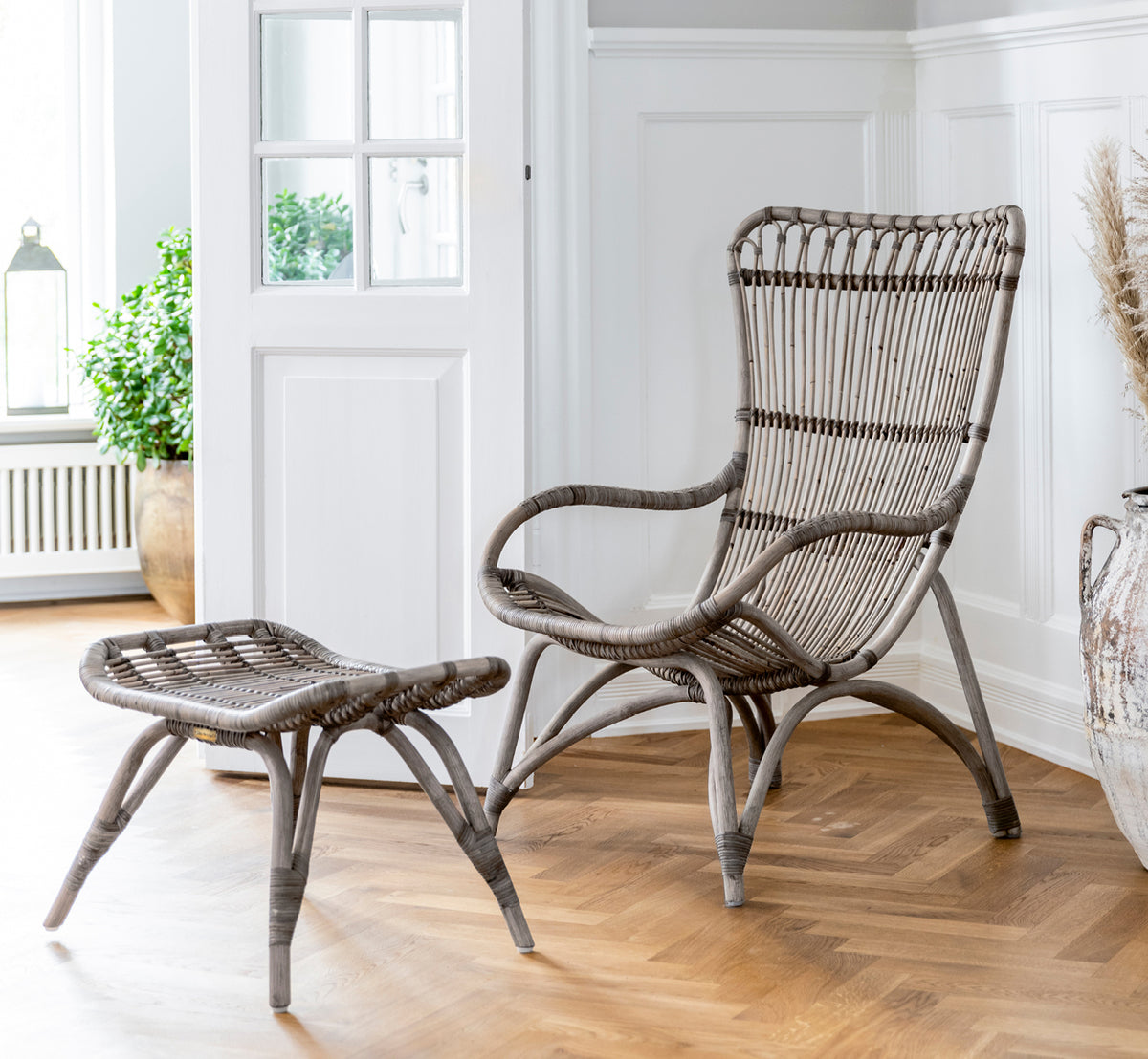 Dette er et livsstilsbillede af Monet Lounge Chair i taupe rattan. Med fodskammel i en mørk ladescene med stearinlys og glasvarer.