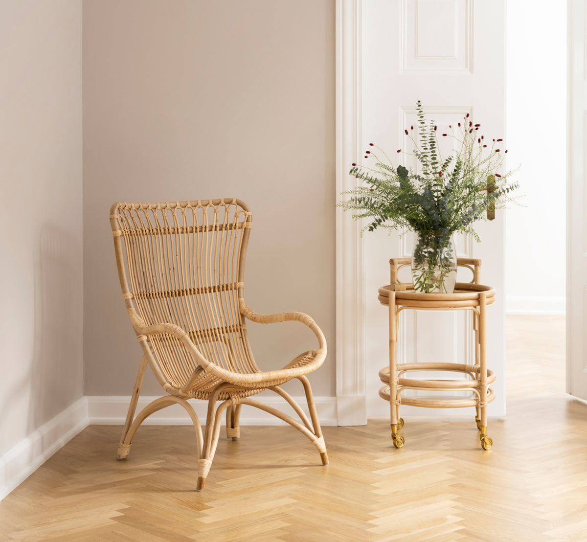 Dette er et livsstilsbillede af Monet Lounge Chair i natural rattan. Med fodskammel og sidebord i en mørk rustik lade med stearinlys.
