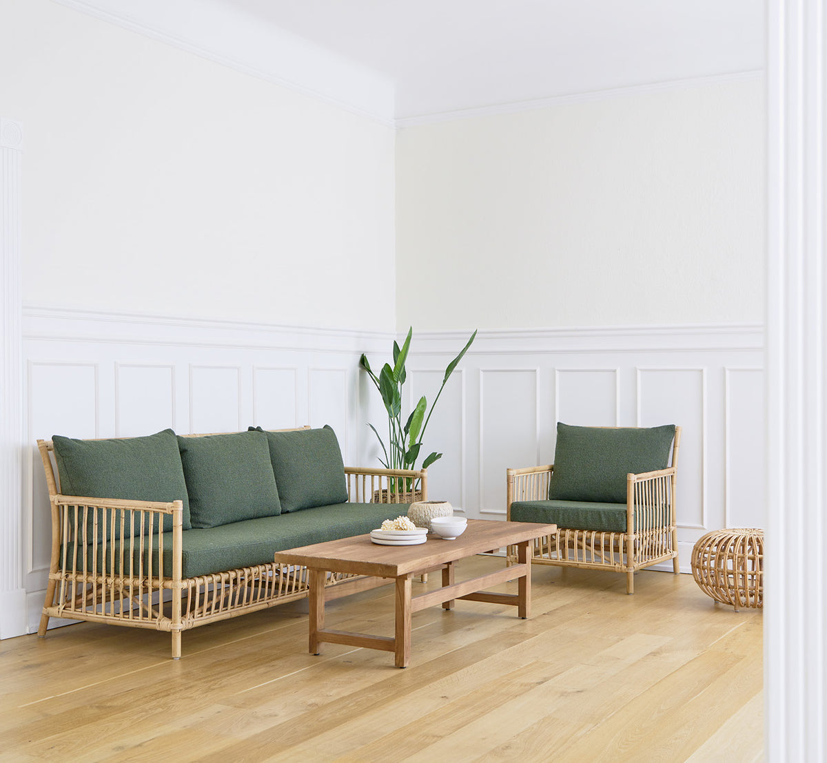 Dette er et livsstilsbillede af Caroline Sofa i natural rattan, i et lyst interiør med hvide panelvægge og sildebensgulv.