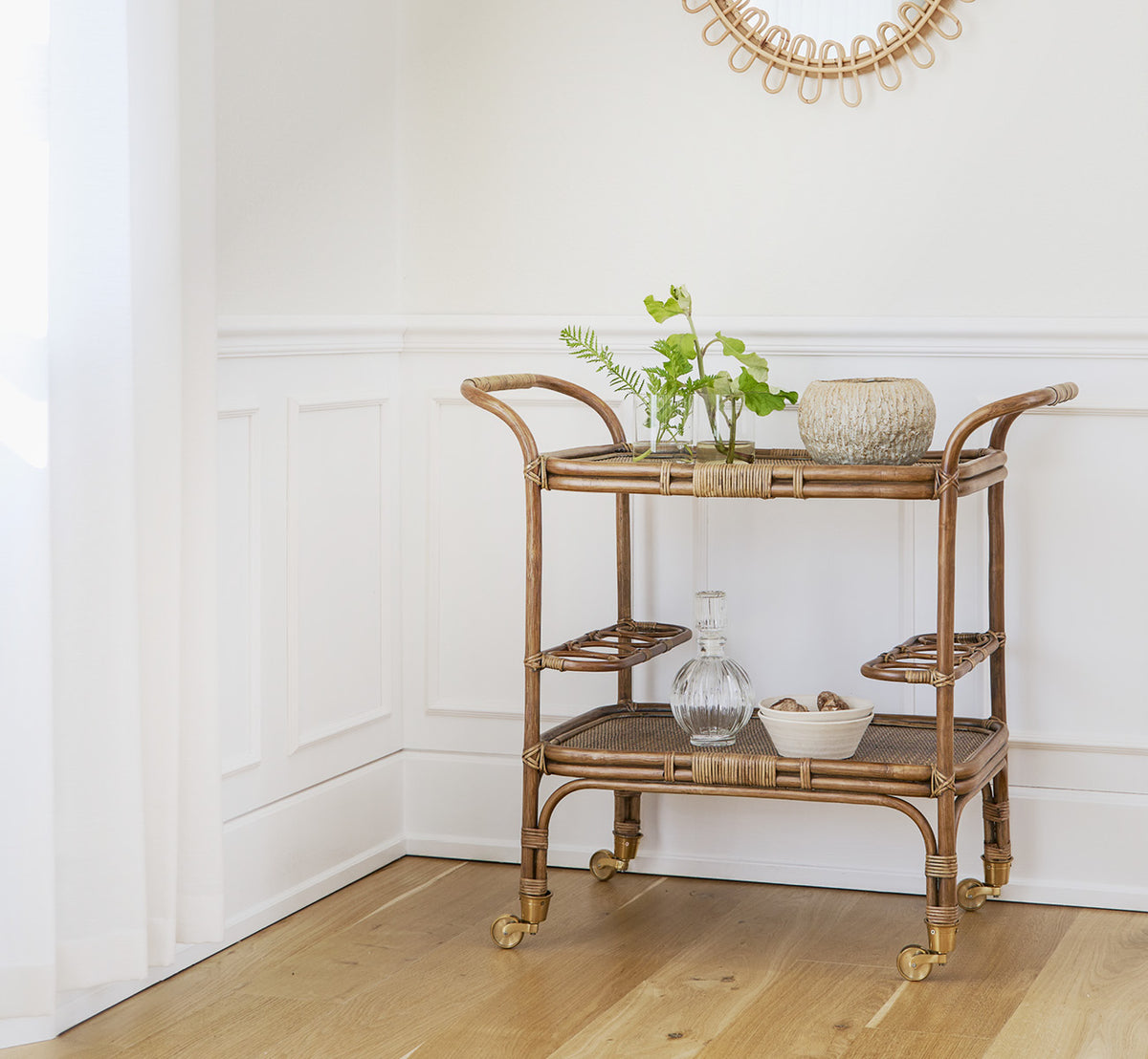 Dette er et livsstilsbillede af Carlo Trolley i antique Rattan, i et lyst hvidt interiør med lambrisering og et rattanspejl på væggen.