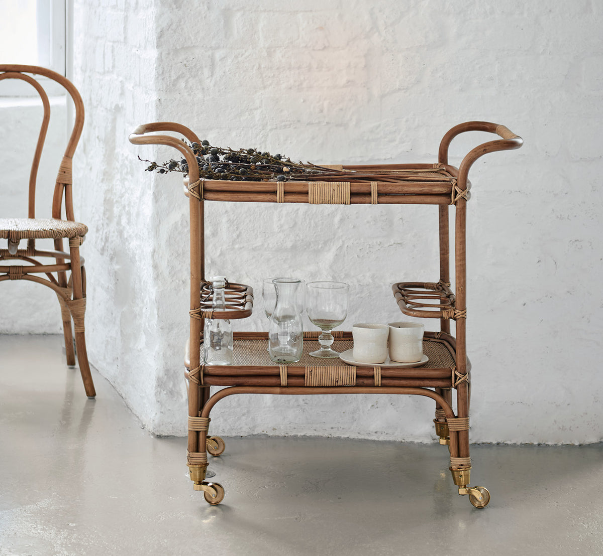 Dette er et livsstilsbillede af Carlo Trolley i antique Rattan, i et lyst hvidt interiør med lambrisering og et rattanspejl på væggen.