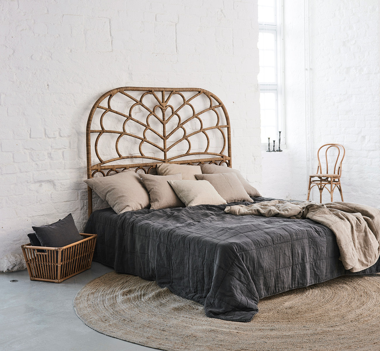 Dette er et livsstilsbillede af Celia Sengegavl i antique rattan, i et roligt lyst soveværelse med neutralt linned og sildebensgulv.