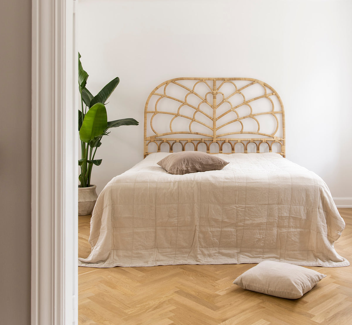 Dette er et livsstilsbillede af Celia Sengegavl i natural rattan, i et roligt lyst soveværelse med neutralt linned og sildebensgulv.