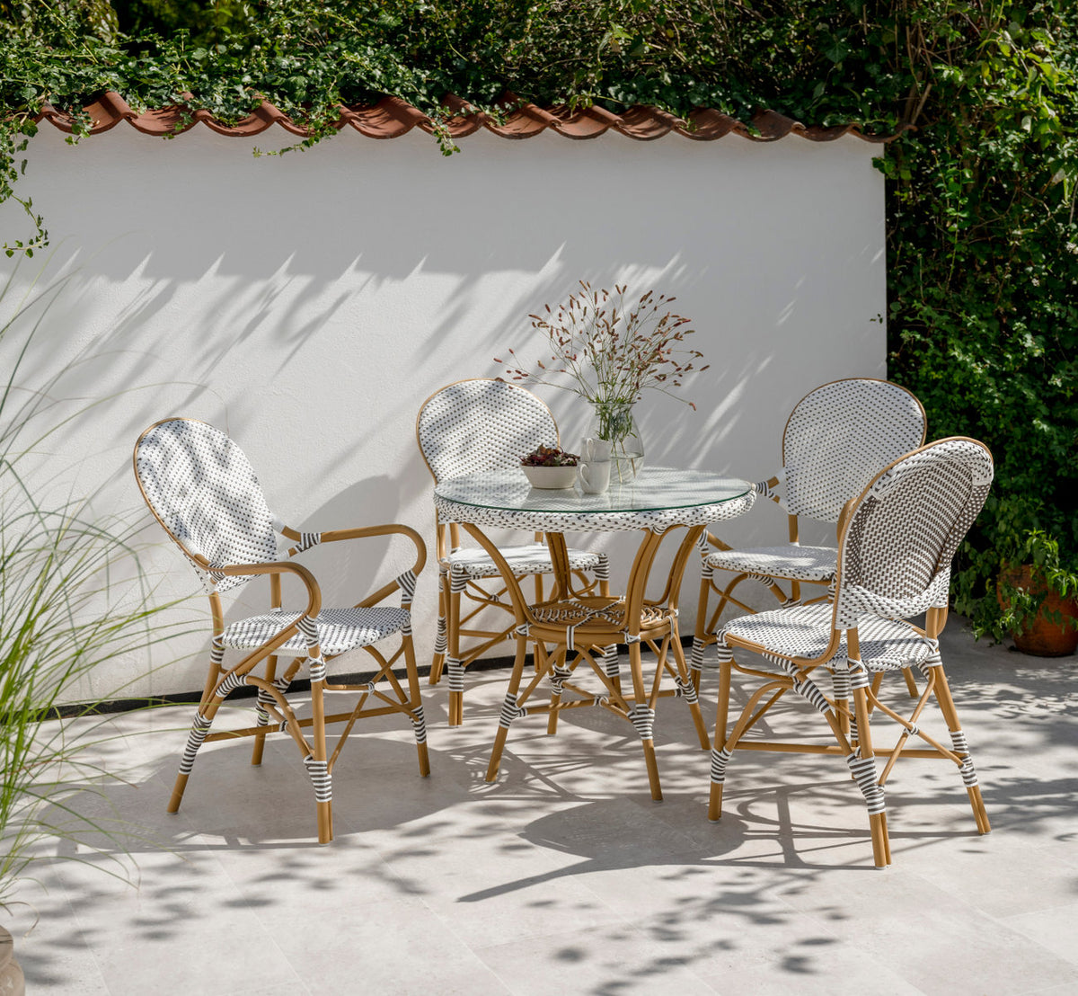 Dette er et livsstilsbillede af Isabell Udendørs spisestuelænestol i almond aluminium frame white w cappuccino dot artfibre. På en solrig terrasse.