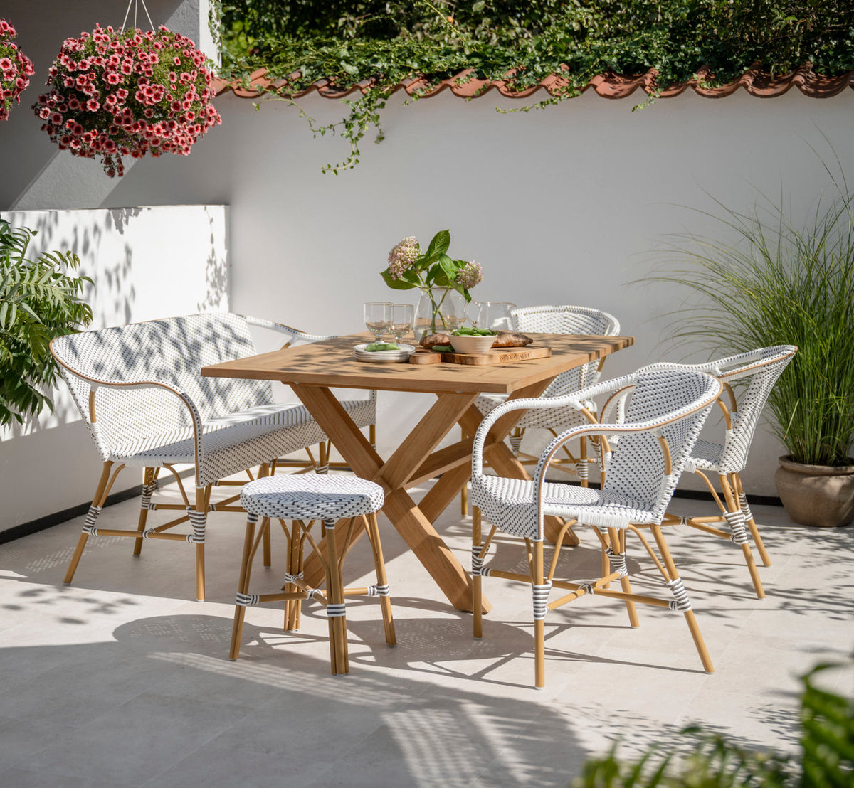 Dette er et livsstilsbillede af Simone Udendørs skammel i almond aluminium frame white w cappuccino dot artfibre. Med teakbord på en solrig terrasse.