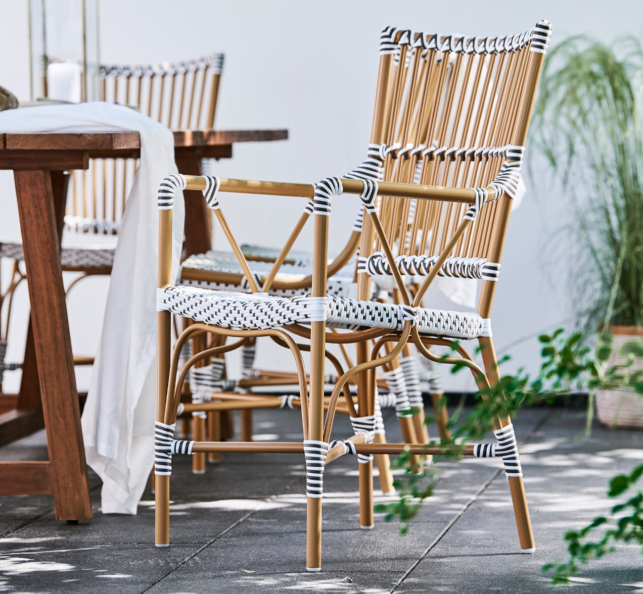 Dette er et livsstilsbillede af Monique Exterior Dining Armchair i white w cappuccino dot ArtFibre. På en solrig terrasse med palmer.