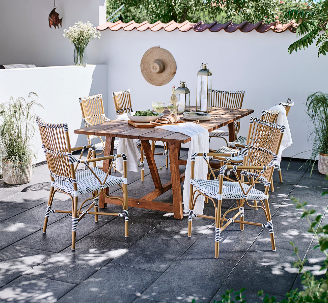 Dette er et livsstilsbillede af Monique Exterior Dining Armchair i white w cappuccino dot ArtFibre. Omkring et teakbord på en terrasse.