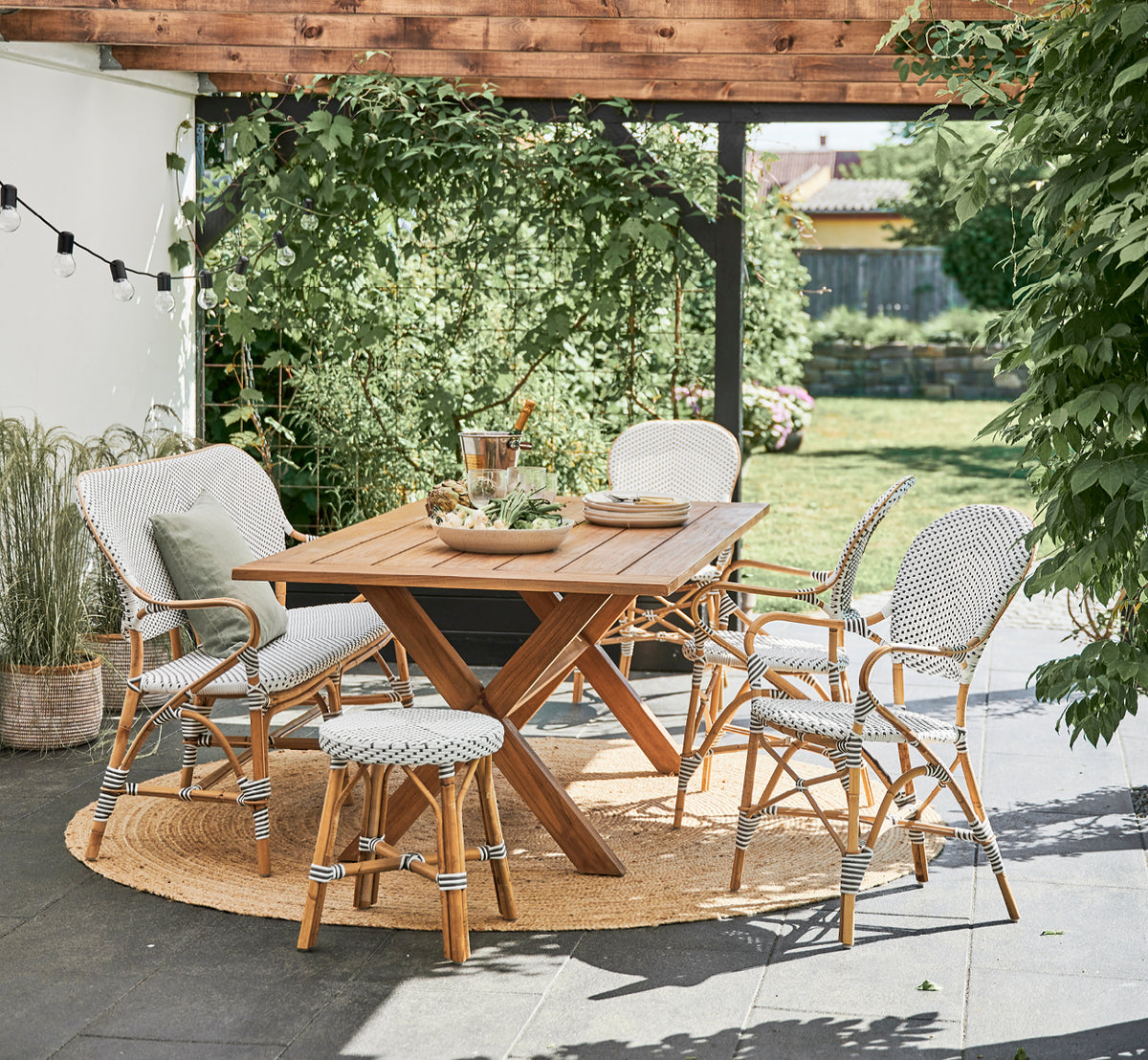Dette er et livsstilsbillede af Simone Skammel i white w cappuccino dot ArtFibre Skin on Rattan frame. Ved et spisebord i teak i haven.