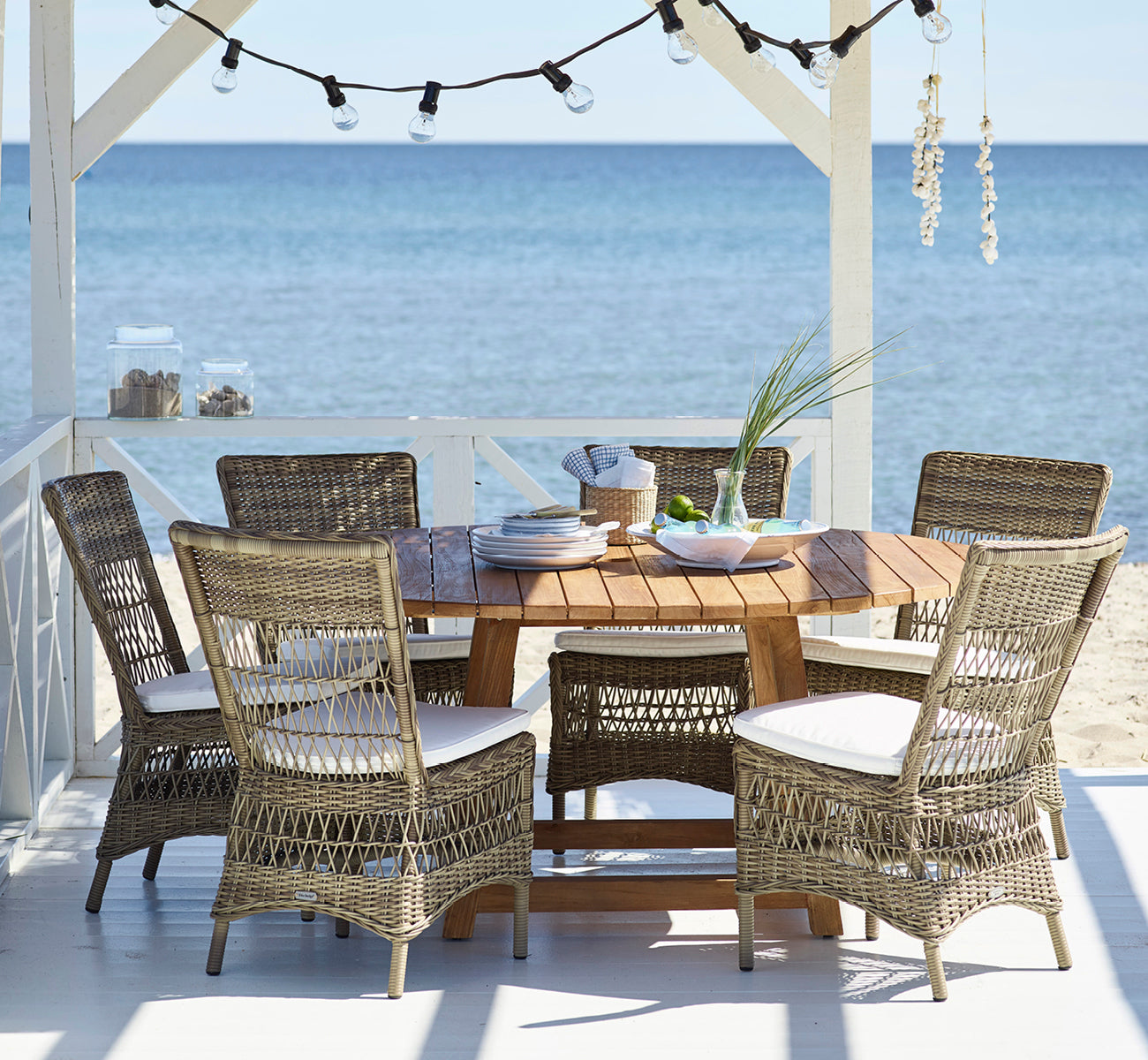 Dette er et livsstilsbillede af Marie Exterior Side Chair i antique grey artfibre aluminium. I en strandpavillon dækket til middag.