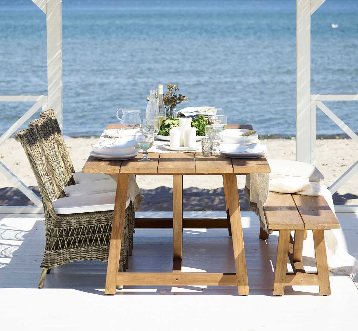 Dette er et livsstilsbillede af Marie Exterior Side Chair i antique grey artfibre aluminium. Ved et teakbord i en strandpavillon.