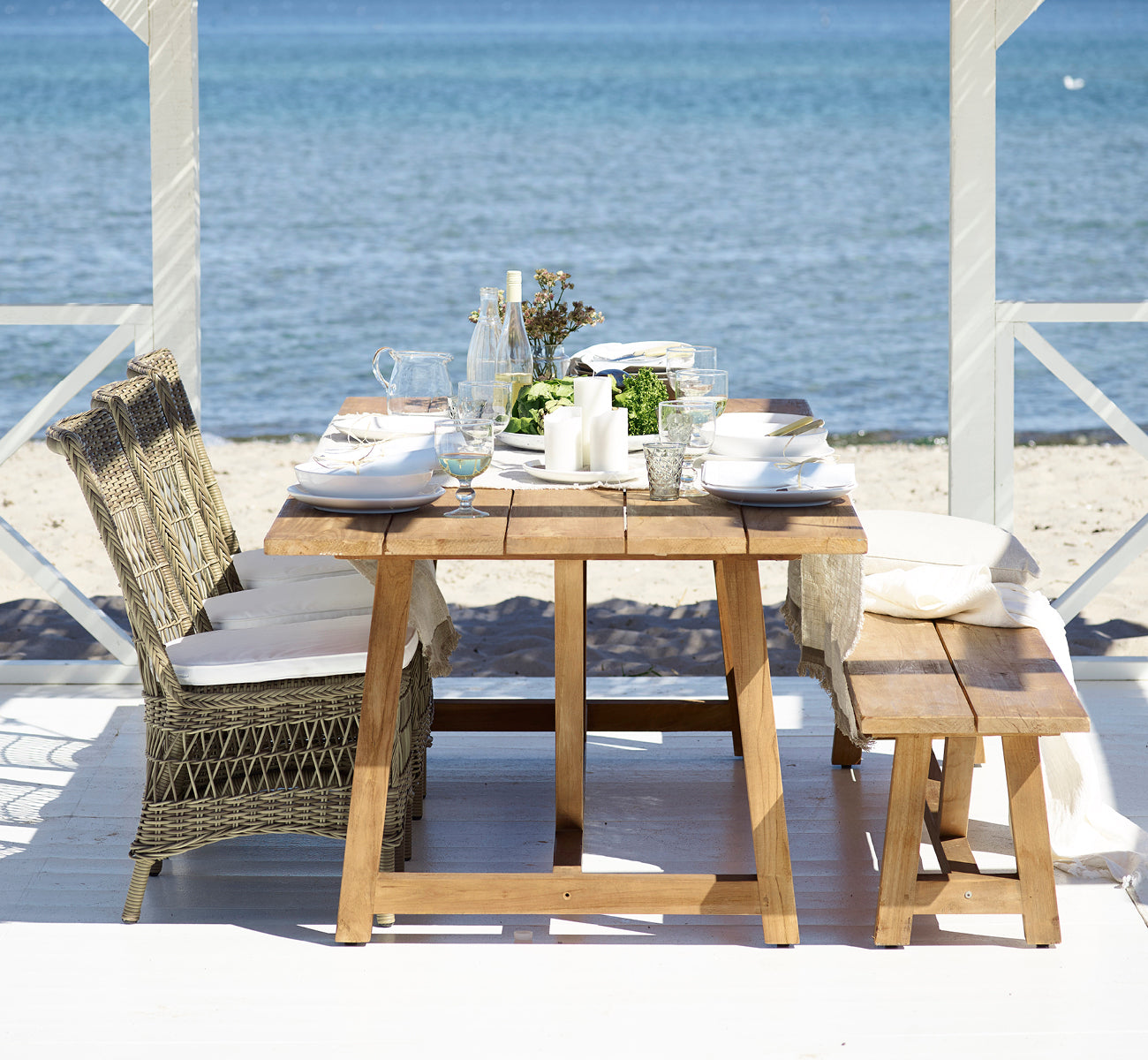 Dette er et livsstilsbillede af Marie Exterior Side Chair i antique grey artfibre aluminium. Ved et teakbord i en strandpavillon.