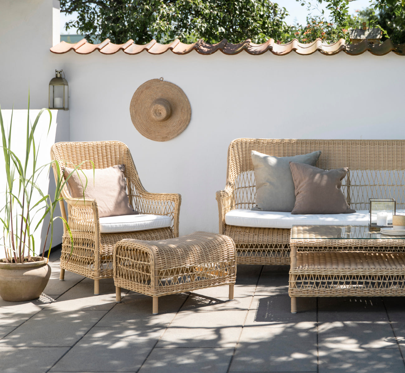 Dette er et livsstilsbillede af Dawn Lænestol i natural ArtFibre Aluminium, på en kystterrasse med havudsigt, strandgræs og hvide søjler.