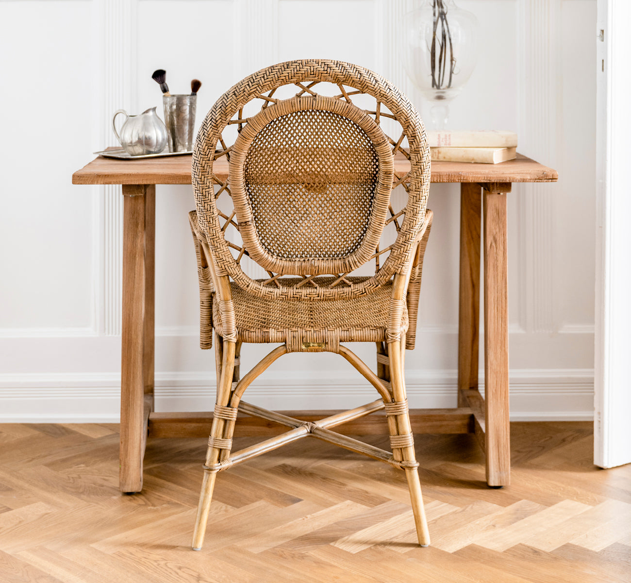 Dette er et livsstilsbillede af Lucas Teak Skrivebord i teak indoor. Placeret mod en grå væg med et teakspejl og pampasgræs i en entré.
