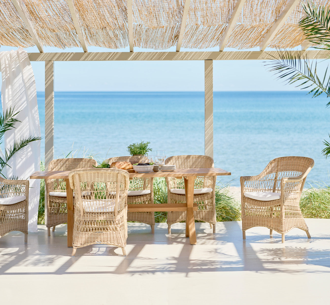 Dette er et livsstilsbillede af Colonial Bord 200 i outdoor Teak, på en strandterrasse med hvidt trædæk og havudsigt.