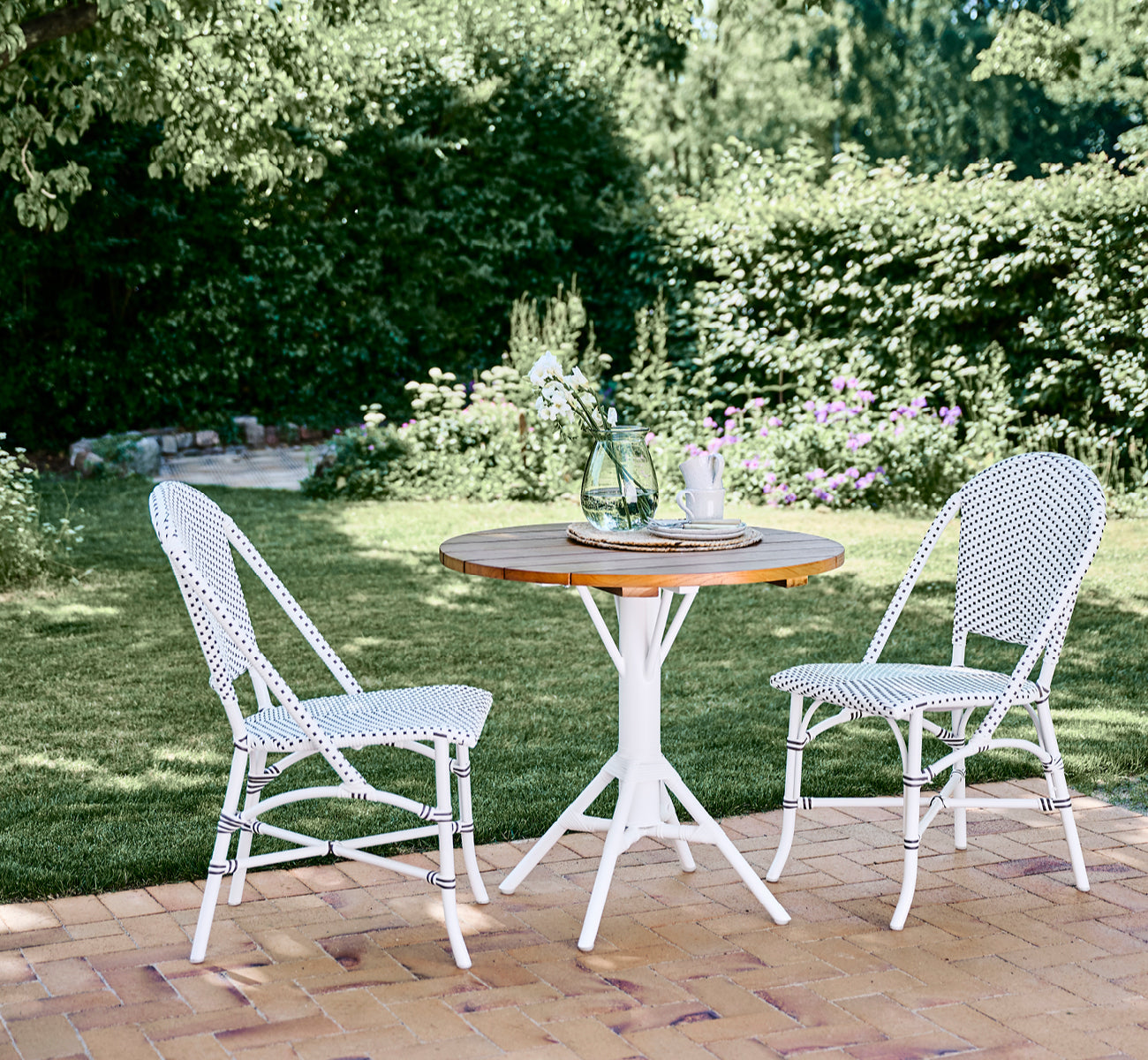 Dette er et livsstilsbillede af Nicole Cafe Table i white aluminium frame white ArtFibre. I en strandpavillon med Piano lænestole.