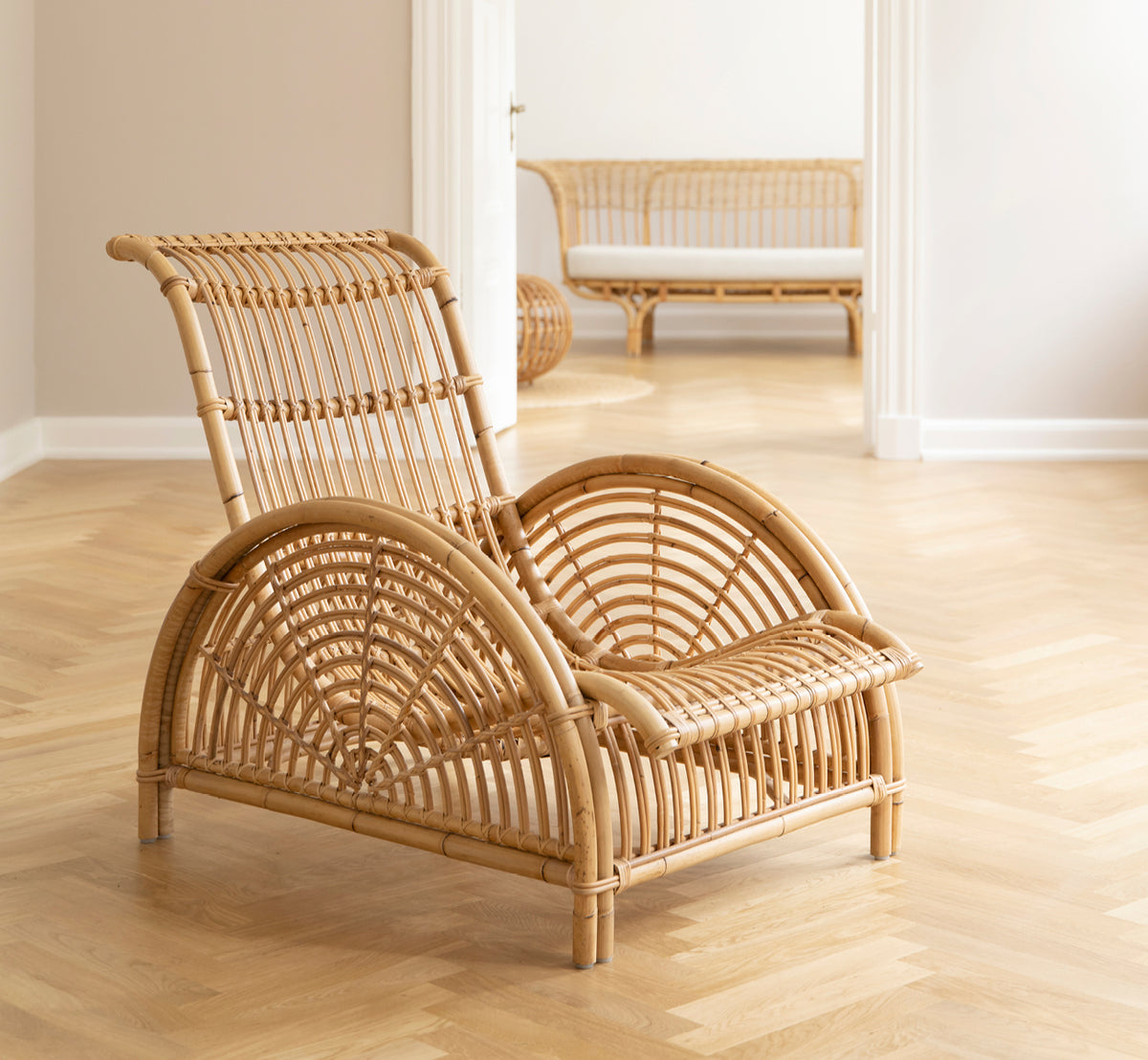 Dette er et livsstilsbillede af Paris Lænestol i polished natural rattan. Placeret på et sildebensparketgulv ved siden af en matchende bænk.