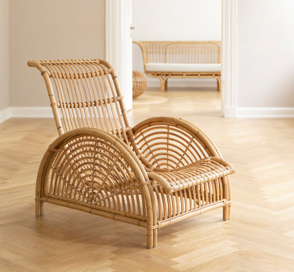 Dette er et livsstilsbillede af Paris Lænestol i polished natural rattan. Placeret på et sildebensparketgulv ved siden af en matchende bænk.