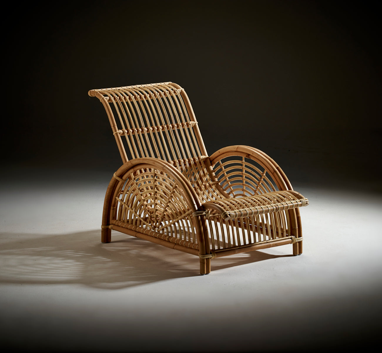 Dette er et livsstilsbillede af Paris Lænestol i polished natural rattan. Placeret på et sildebensparketgulv ved siden af en matchende bænk.