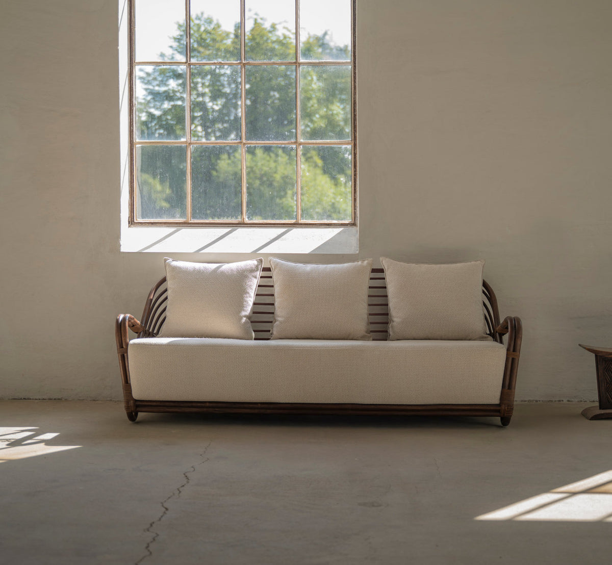 Dette er et livsstilsbillede af Charlottenborg 3-personers sofa i brown rattan. Med linnedpuder ved et stort vindue.