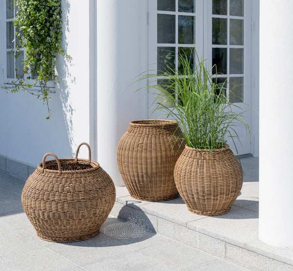 Dette er et livsstilsbillede af Ellis Kurv i chestnut core weave ArtFibre Aluminium, udendørs på en solbeskint terrasse med hvid mur og flisegulv.
