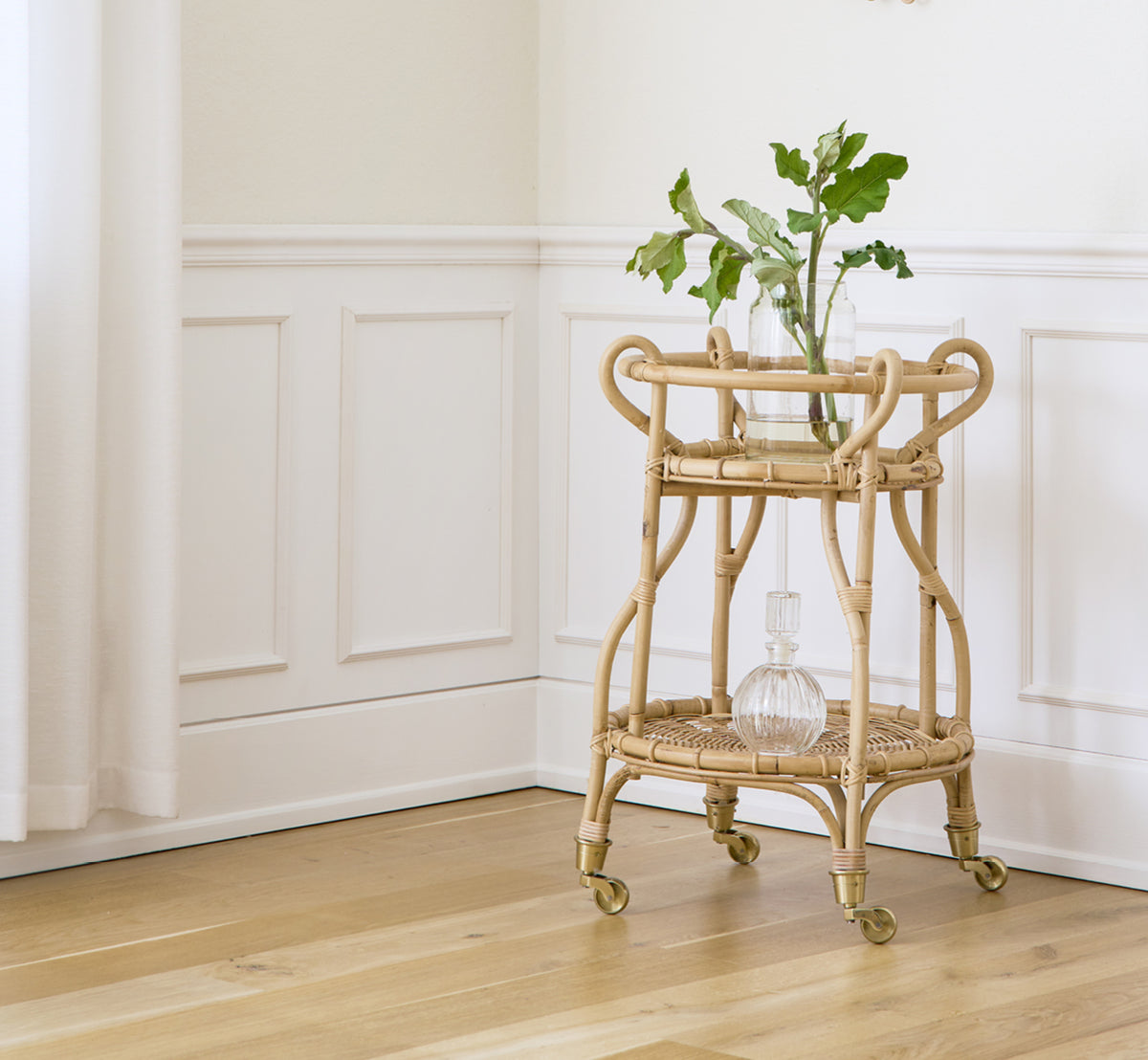Dette er et livsstilsbillede af Fratellino Serveringsvogn i polished Natural Rattan, i et klassisk interiør med forseggjorte hvide paneldøre.