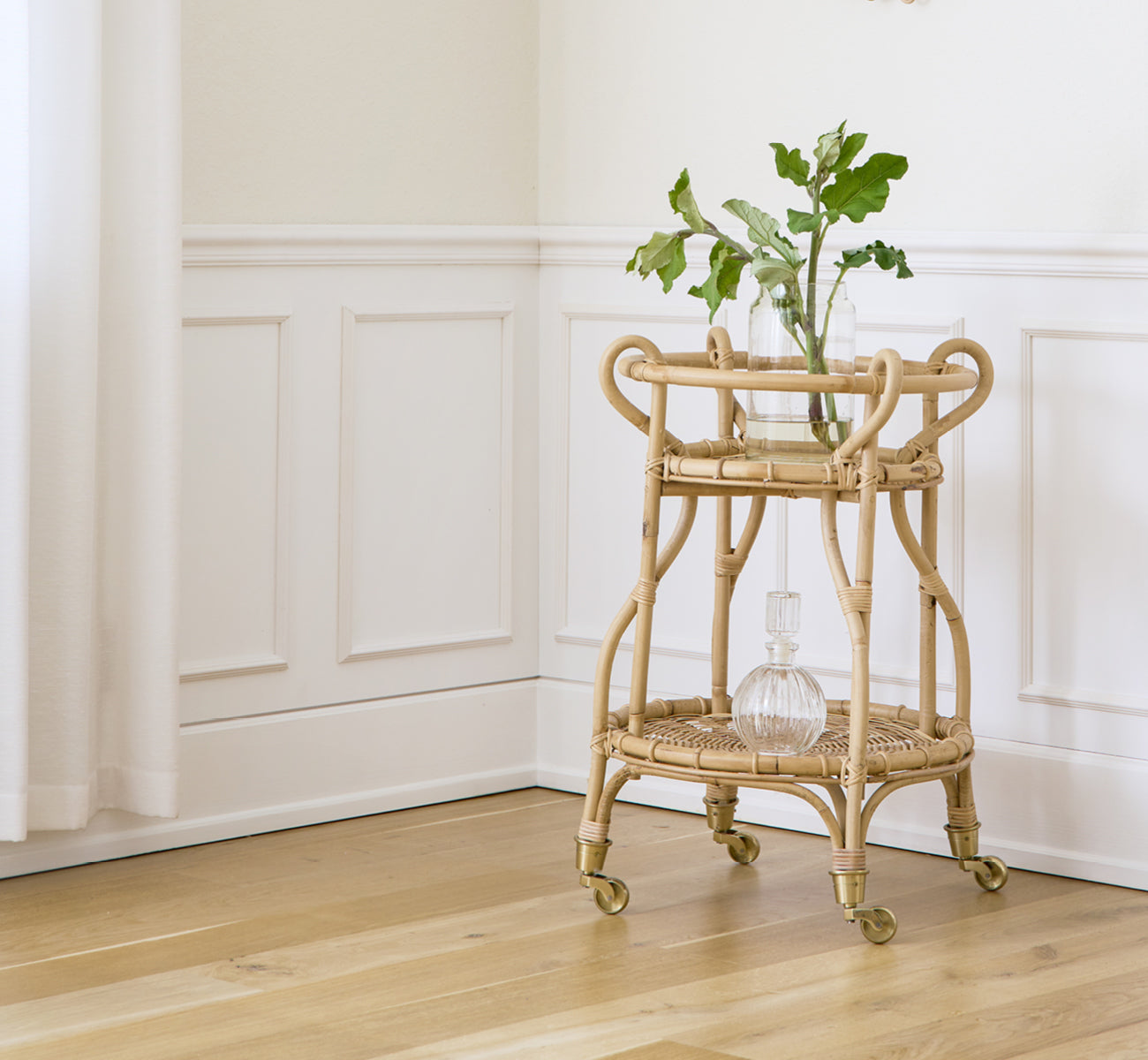 Dette er et livsstilsbillede af Fratellino Serveringsvogn i polished Natural Rattan, i et klassisk interiør med forseggjorte hvide paneldøre.