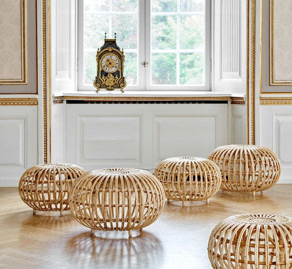 Dette er et livsstilsbillede af Ottoman Small i natural skin on rattan. Samlet i et klassisk panelinteriør med et antikt ur.