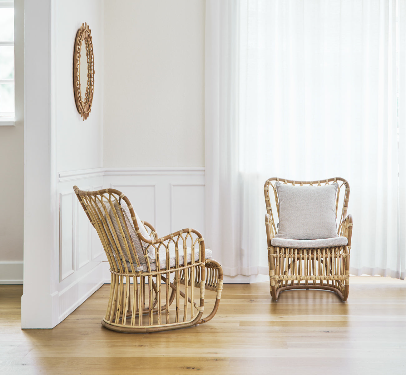 Dette er et livsstilsbillede af Tulip Lænestol i polished natural rattan. Kombineret med en matchende sofa i et lyst panelrum med dør.