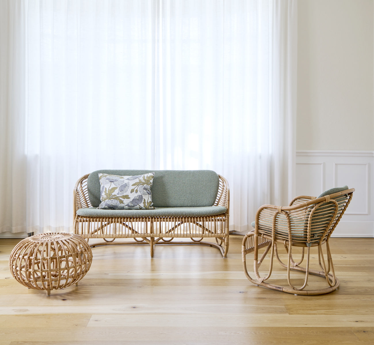 Dette er et livsstilsbillede af Swing Lænestol i polished natural rattan. Stående alene ved siden af en løvrig plante på et sildebensparketgulv.