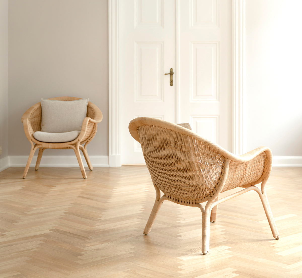 Dette er et livsstilsbillede af Madame Lænestol i natural core weave rattan frame. Lyst rum med sildebensgulv og hvide dobbeltdøre.