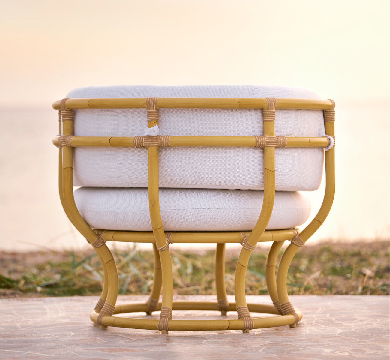 Dette er et livsstilsbillede af Coco Udendørs lænestol i natural Aluminium ArtFibre, på en åben kystterrasse ved solnedgang med havudsigt.